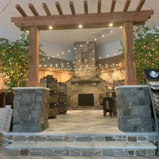 Stone-walled interior with fireplace, overhead lights, wood pergola entrance, and faux greenery.