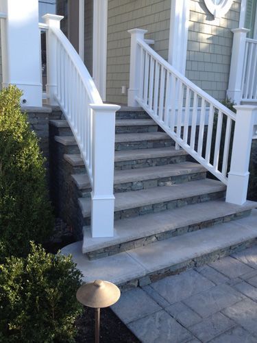 White-railed stairs leading up to a house entrance. Stone steps and base.