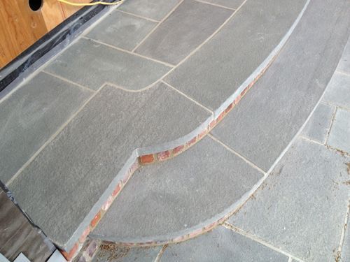 Stone patio with steps, gray stone, brick trim, curved edge, outdoor setting.