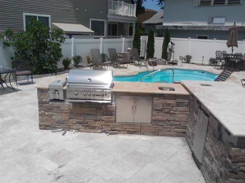 Outdoor kitchen with a grill, sink, and storage next to a pool.
