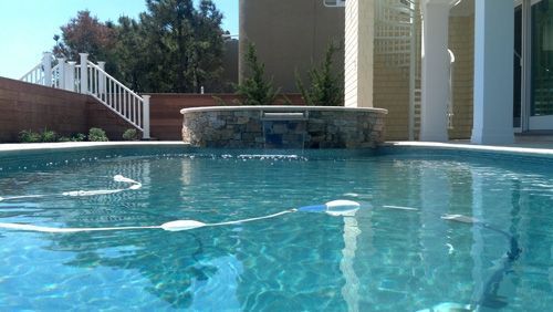 Swimming pool with a stone waterfall feature, steps, and a white railing in a backyard setting.
