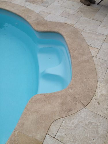 Swimming pool with integrated steps, surrounded by stone tile. Blue water reflects light.
