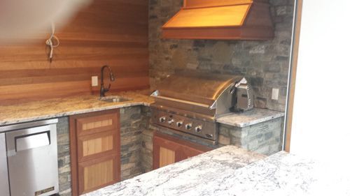 Outdoor kitchen with granite countertops, stainless steel grill, and wooden cabinets.