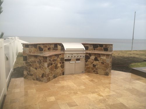 Outdoor kitchen with stone facade and grill, overlooking water.