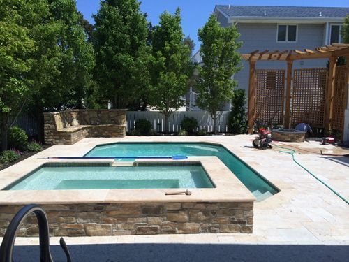 Backyard pool and spa area with stone surround, patio, and pergola.