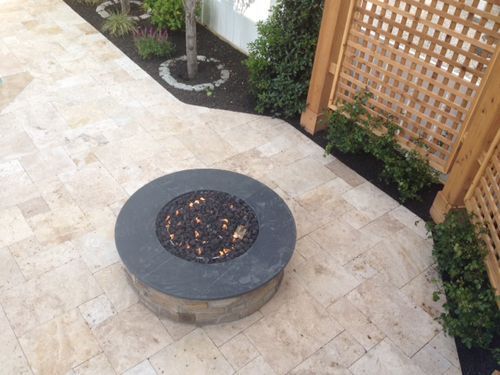 Circular fire pit on a stone patio with a wooden trellis and landscaped garden.