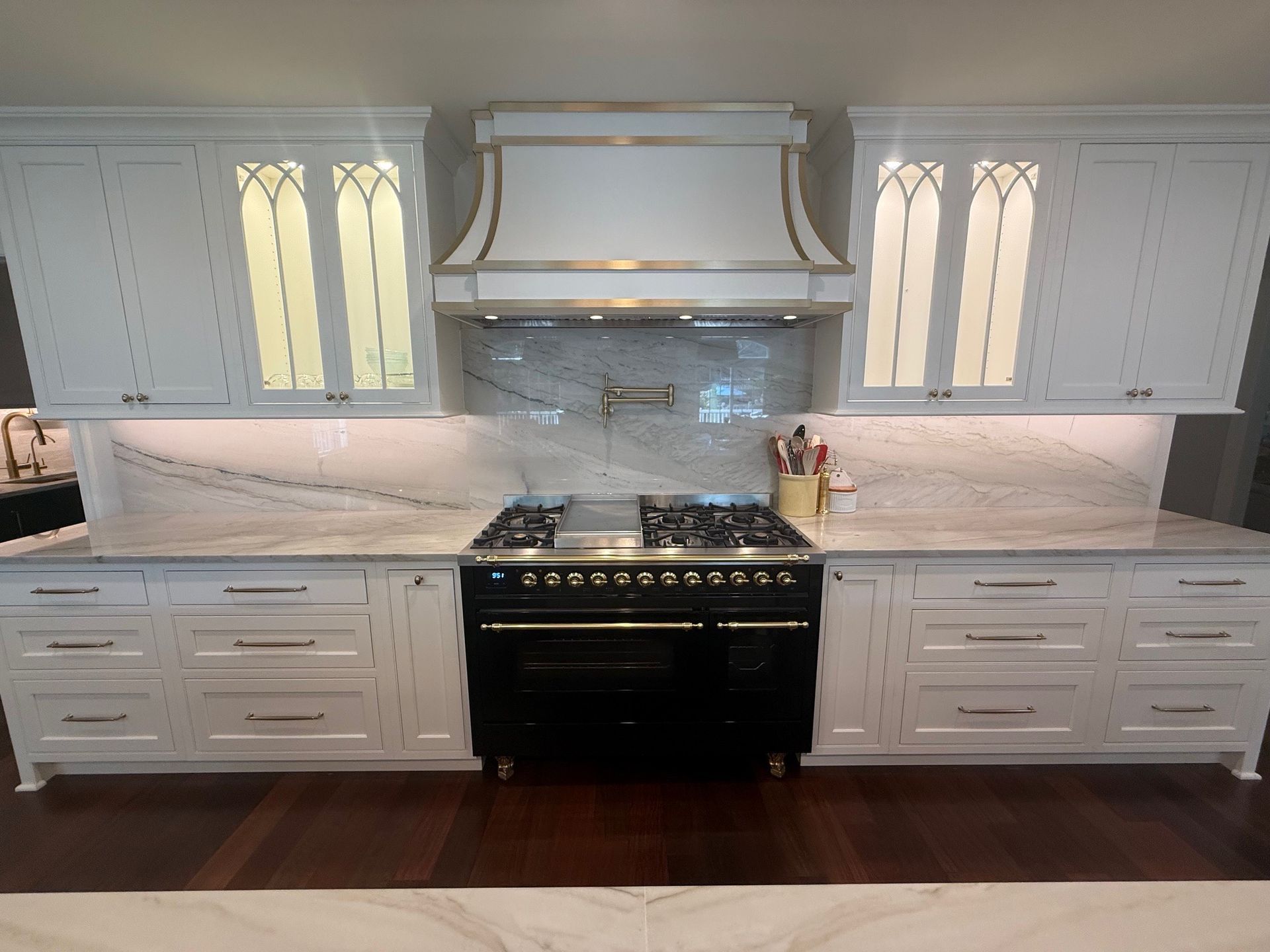 White kitchen with black stove, marble countertops, and cabinets.