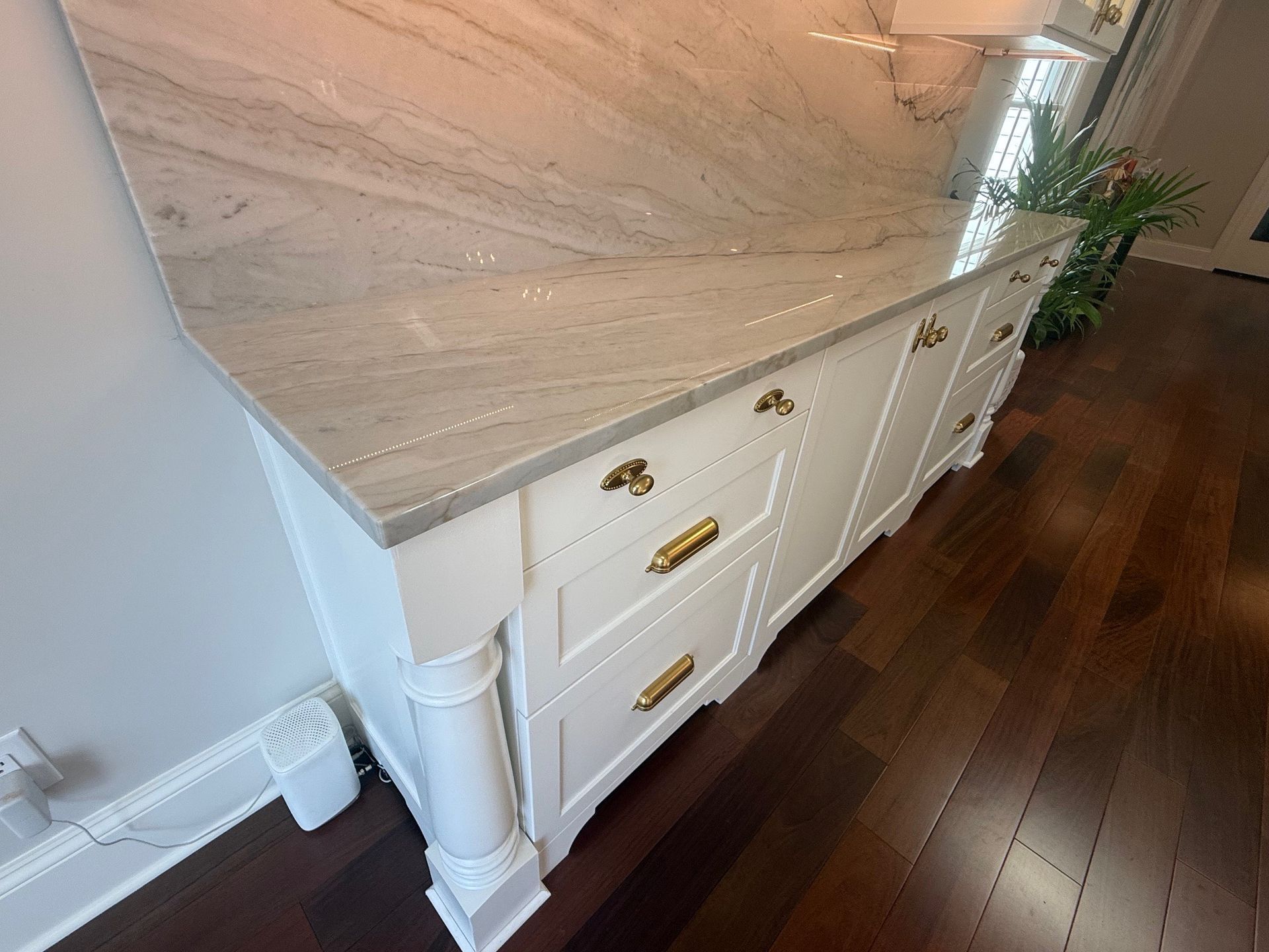 White kitchen island with marble countertop and brass hardware against dark wood flooring.