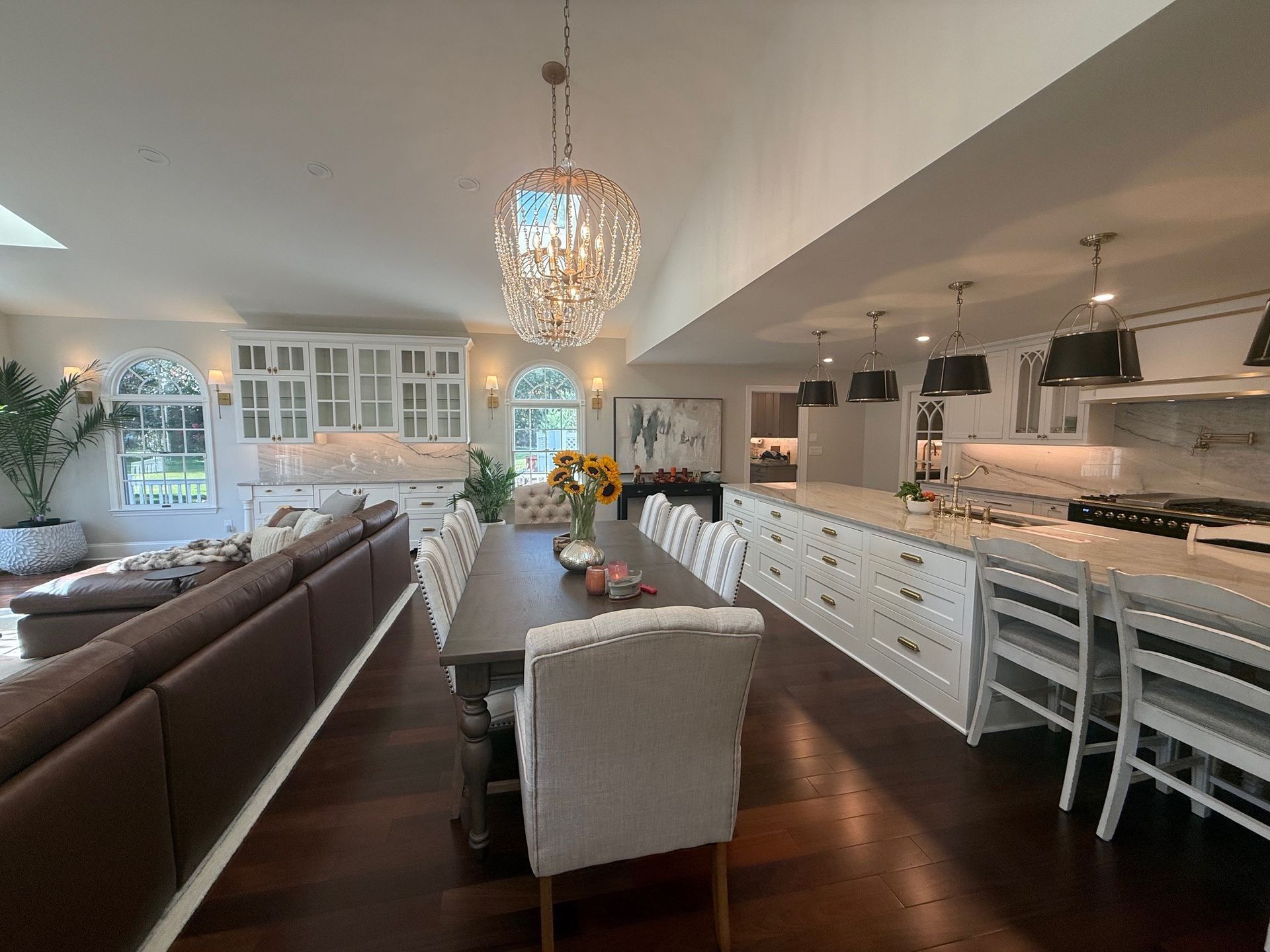Spacious, open-concept kitchen and dining area with long table, white cabinets, and ornate chandelier.