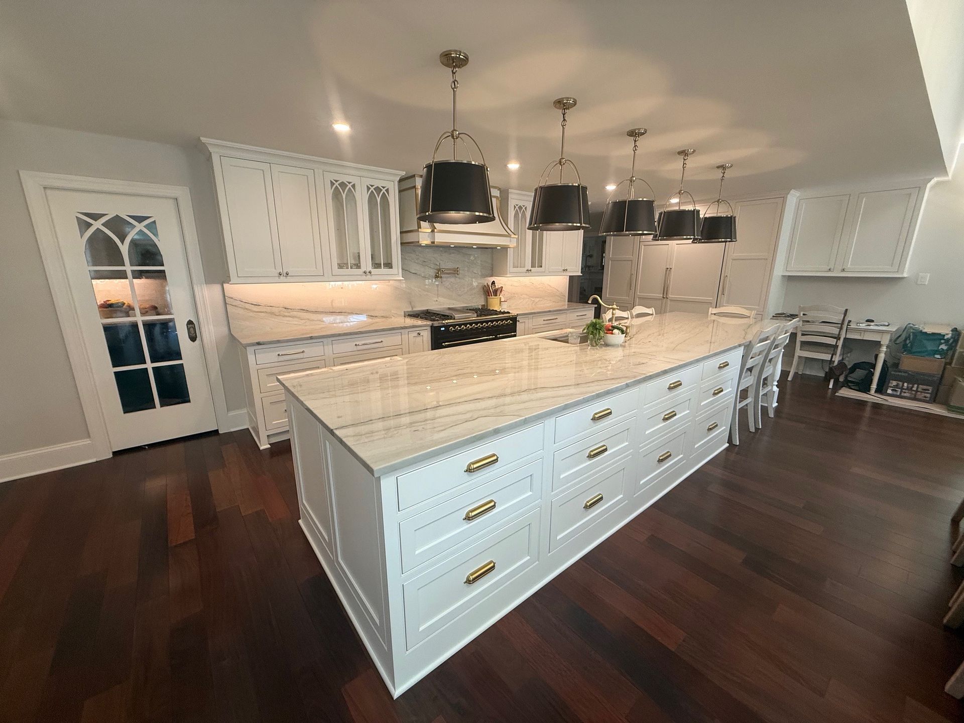 White kitchen with large island, marble countertops, pendant lights, dark wood floors.