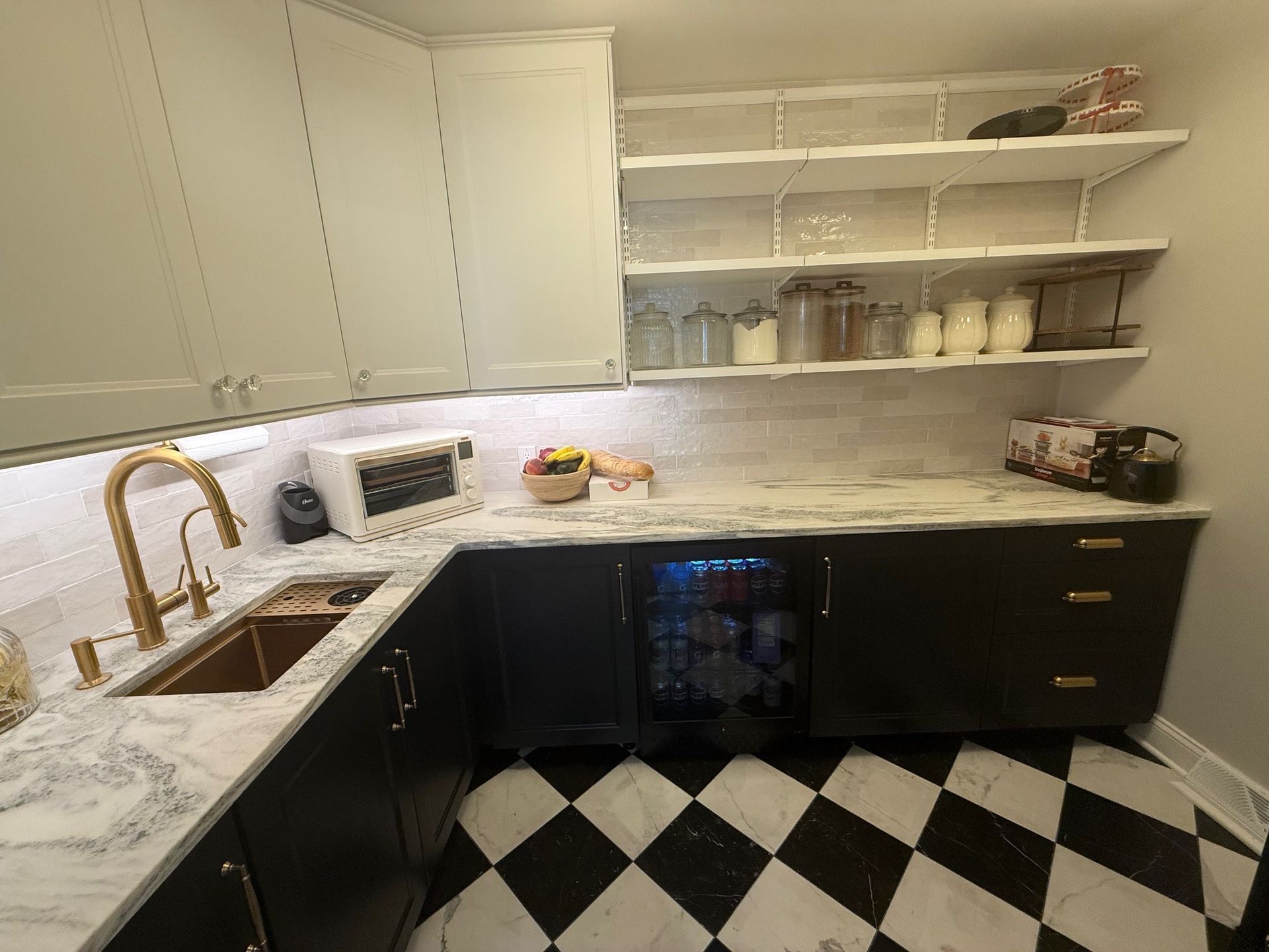 Kitchen pantry with black and white checkered floor, marble counters, black cabinets, and open shelving.