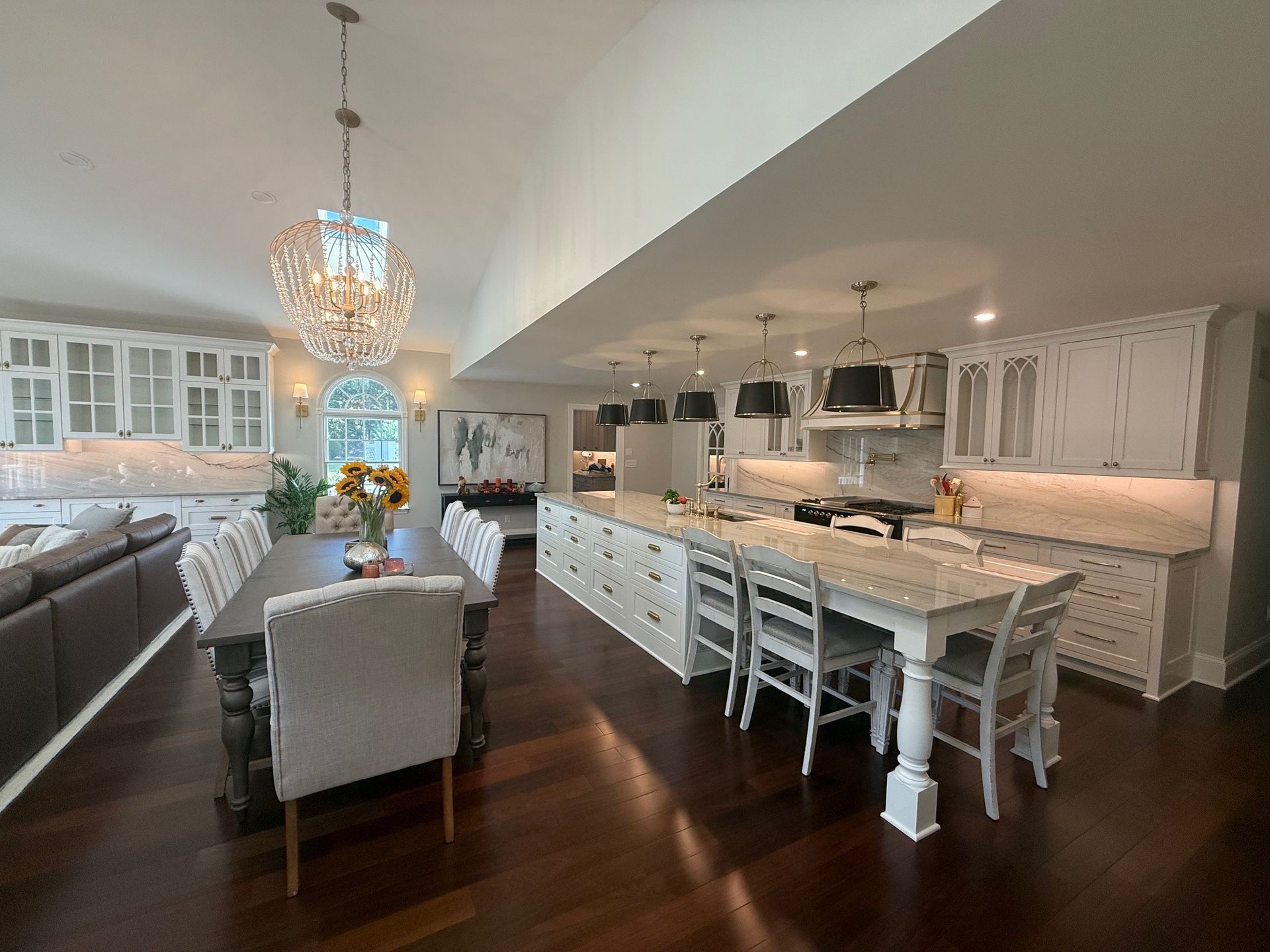 Spacious white kitchen with dark wood floors, large island with seating, dining table, and chandelier.