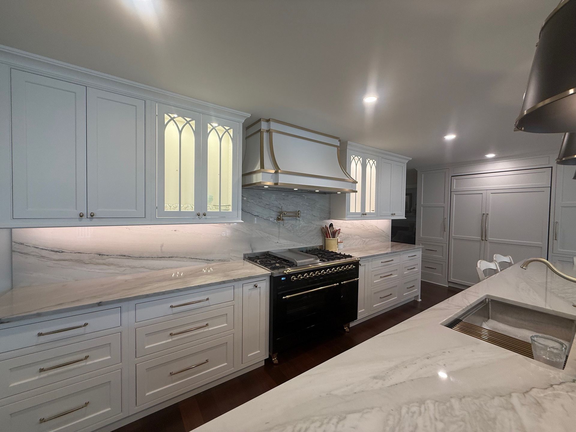 White kitchen with marble countertops, stainless steel range hood, and black stove.