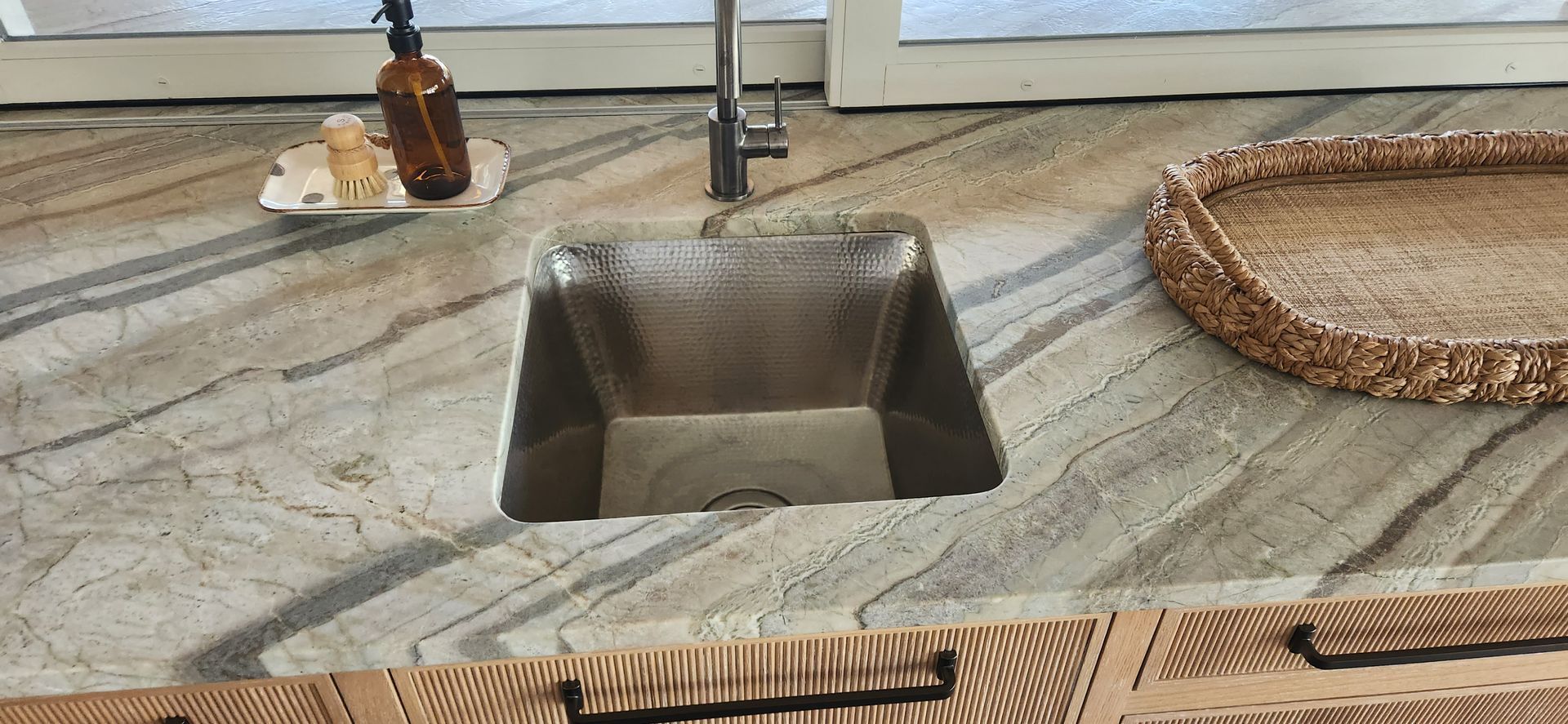 Kitchen sink with countertop, soap, and a woven basket.