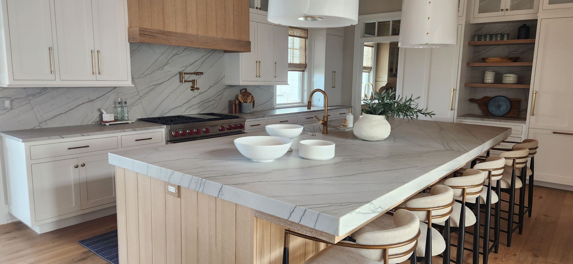 Kitchen with white cabinets, light wood island with stools, marble backsplash, and a large light fixture.