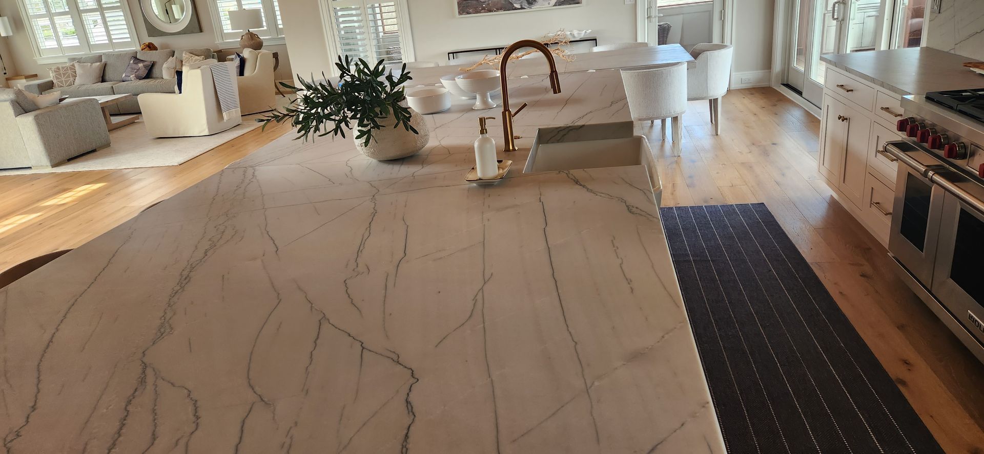 Kitchen island with veined countertop, bronze faucet, hardwood floors, and rug.