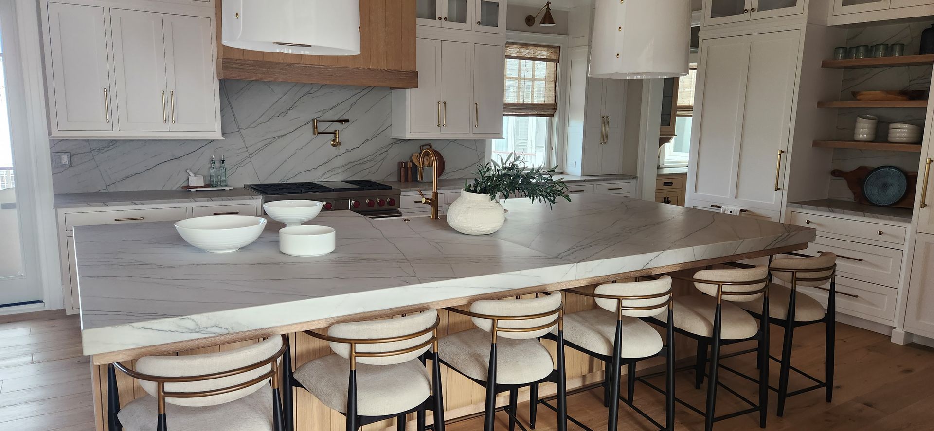 Kitchen with a large island with bar stools. White cabinets, marble backsplash, and wooden accents.