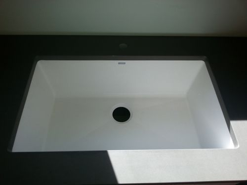 White rectangular bathroom sink set in a gray countertop, with a single faucet hole.
