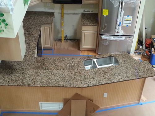 Granite countertop in kitchen with a sink, two cabinets, and stainless steel refrigerator.