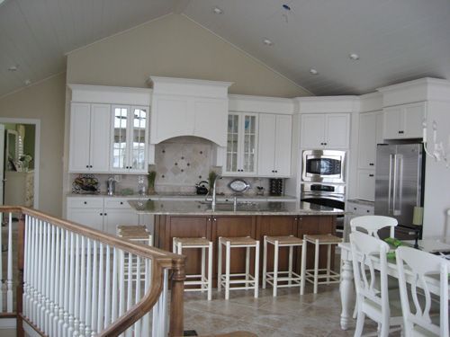 White kitchen with island and brown cabinets, stainless steel appliances, and a staircase.
