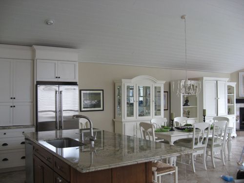 Kitchen with large island, white cabinets, stainless steel refrigerator, dining area, white furniture.