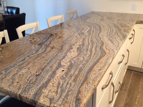 Granite countertop with swirled patterns. Light and dark brown tones. White cabinets and chairs are present.