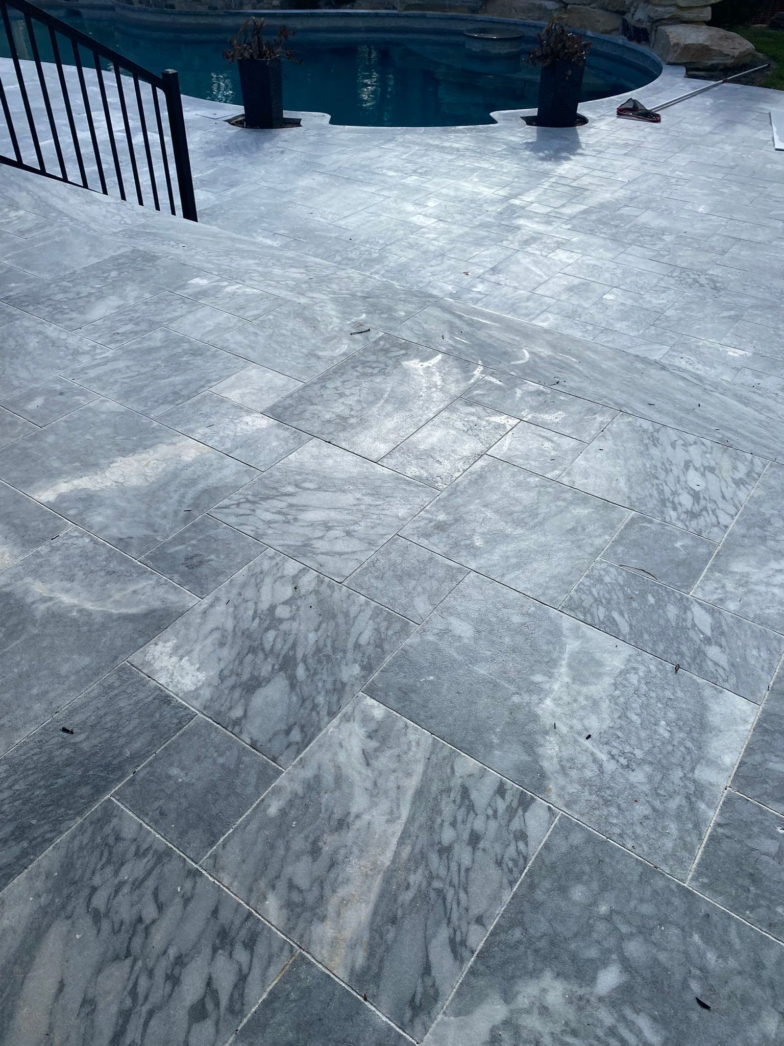 Gray marble patio with pool in the background, black metal railing on the left.