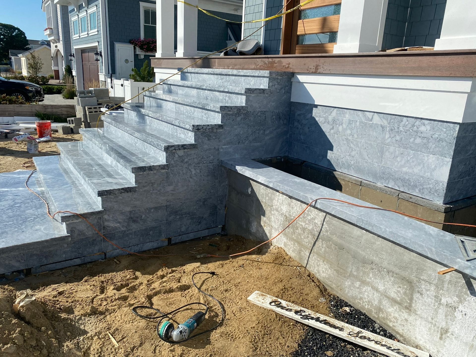 Gray stone steps under construction leading to a house entrance. Sand, tools, and concrete are also visible.