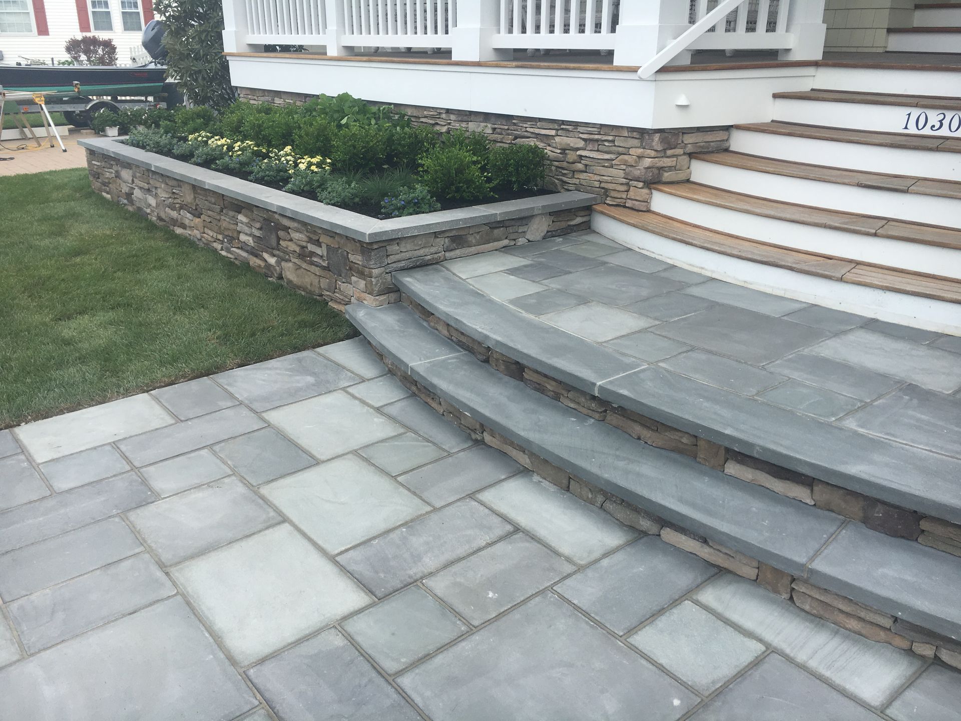 Stone walkway and steps leading to a house with a raised garden bed and white porch.