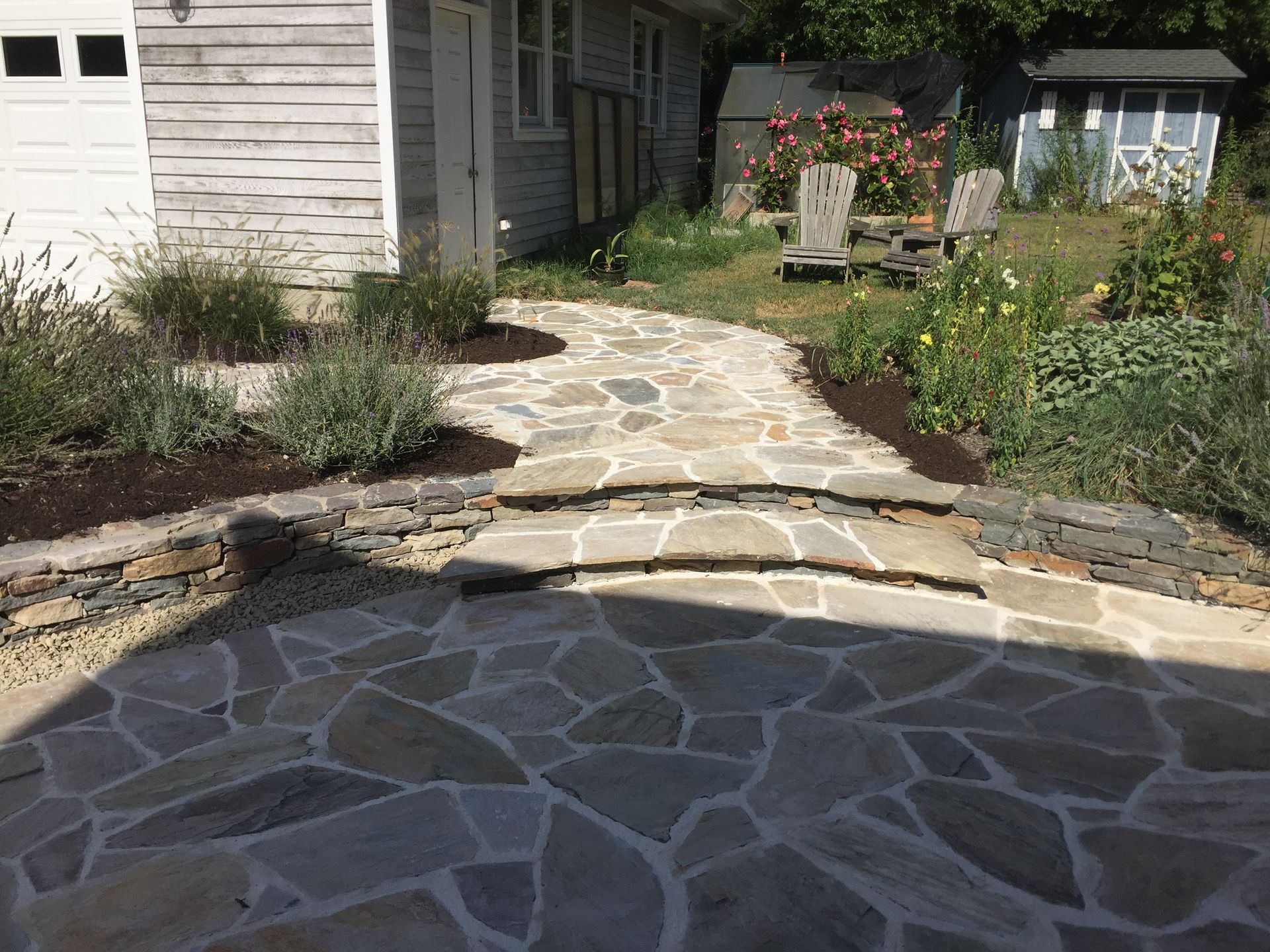 Stone pathway with steps leading to a house. Landscaping with plants and mulch borders.