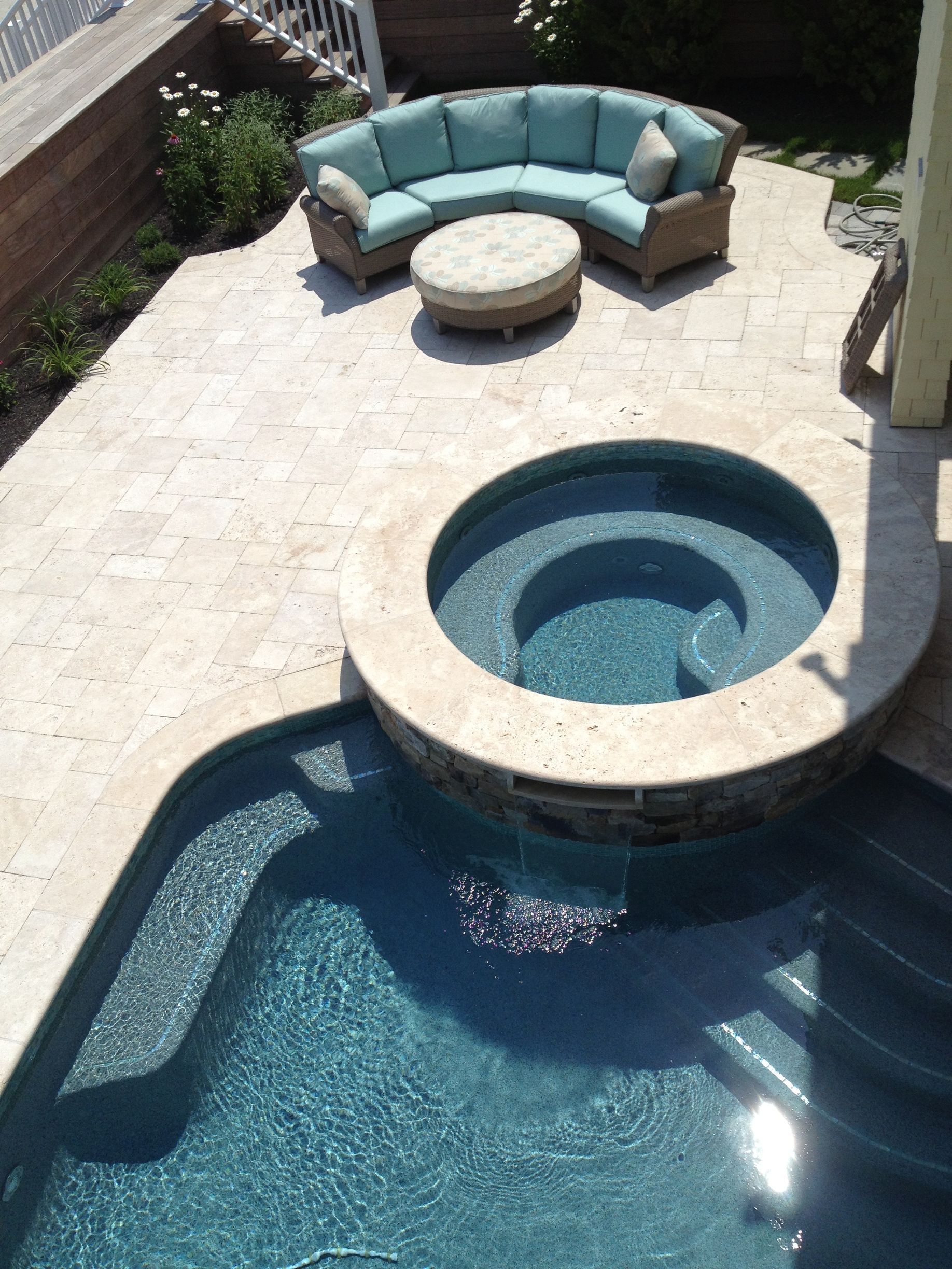 Pool and spa area with blue water, beige patio, and teal sectional seating.
