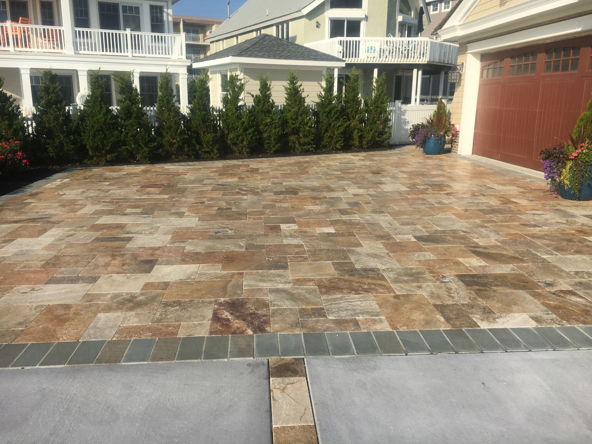 Driveway paved with patterned stone, bordered by a blue-gray brick. Green trees line the edge.