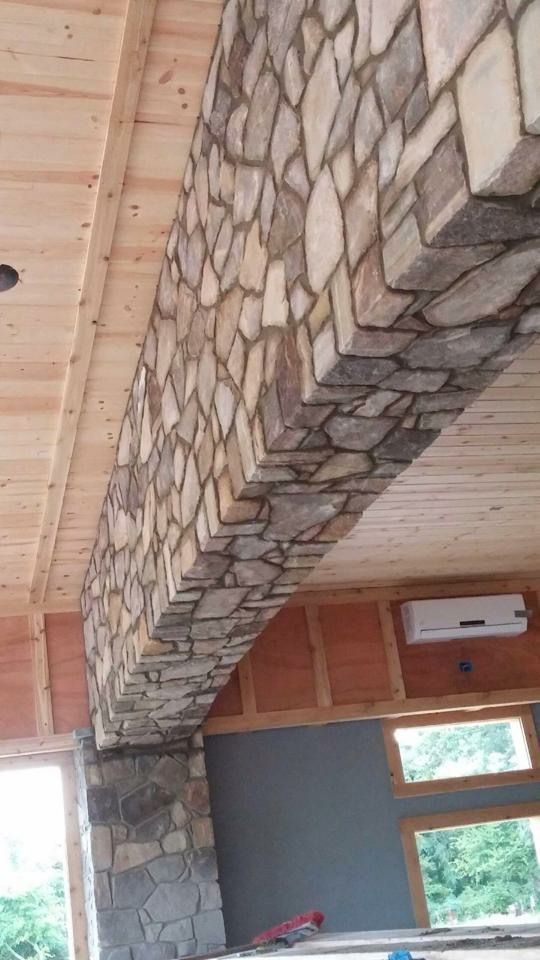 Stone-covered structural beam in a room with wood ceiling and cabinetry, and windows overlooking greenery.