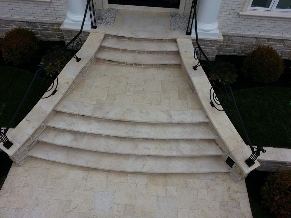 Stone steps leading up to a white building's entrance. Black railings and manicured shrubs are visible.