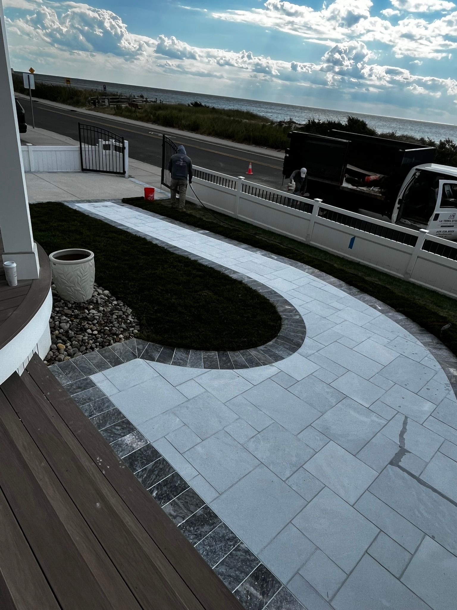 Curving paved walkway leading from a deck, with grass and ocean view.