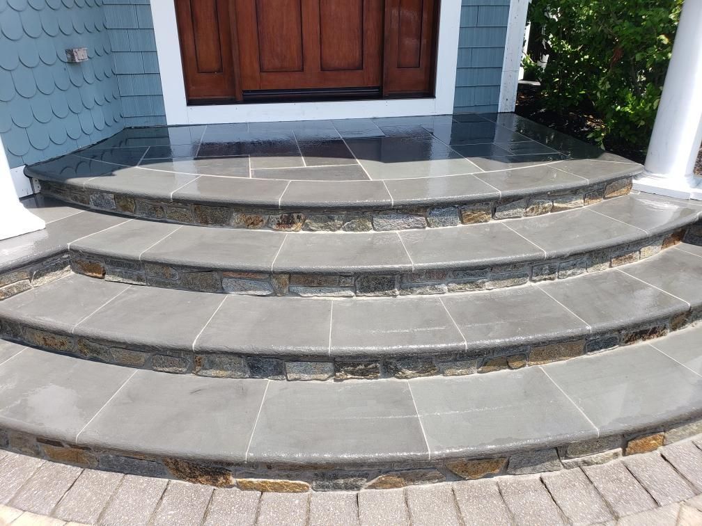 Curved stone steps leading up to a wooden door, with brick and white pillar supports.