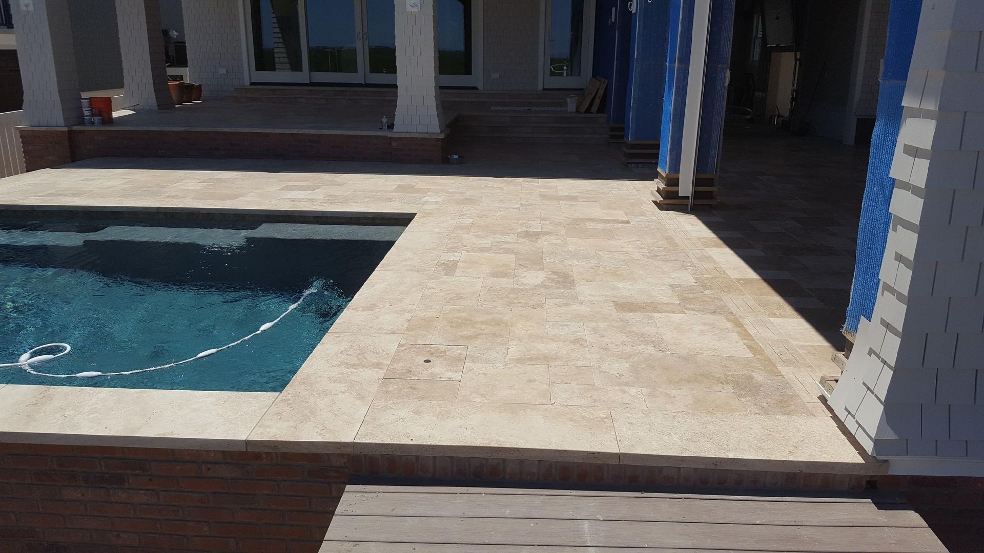 Poolside patio with travertine pavers, pool, and covered porch.