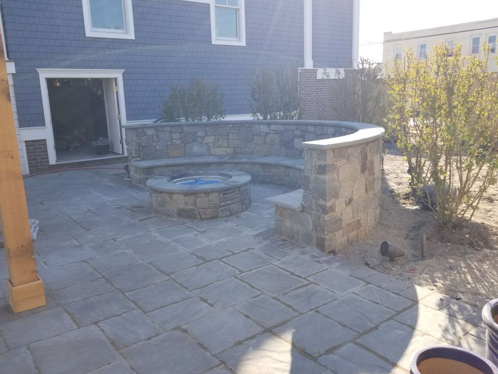Stone patio with a curved stone bench, fire pit, and building in the background.