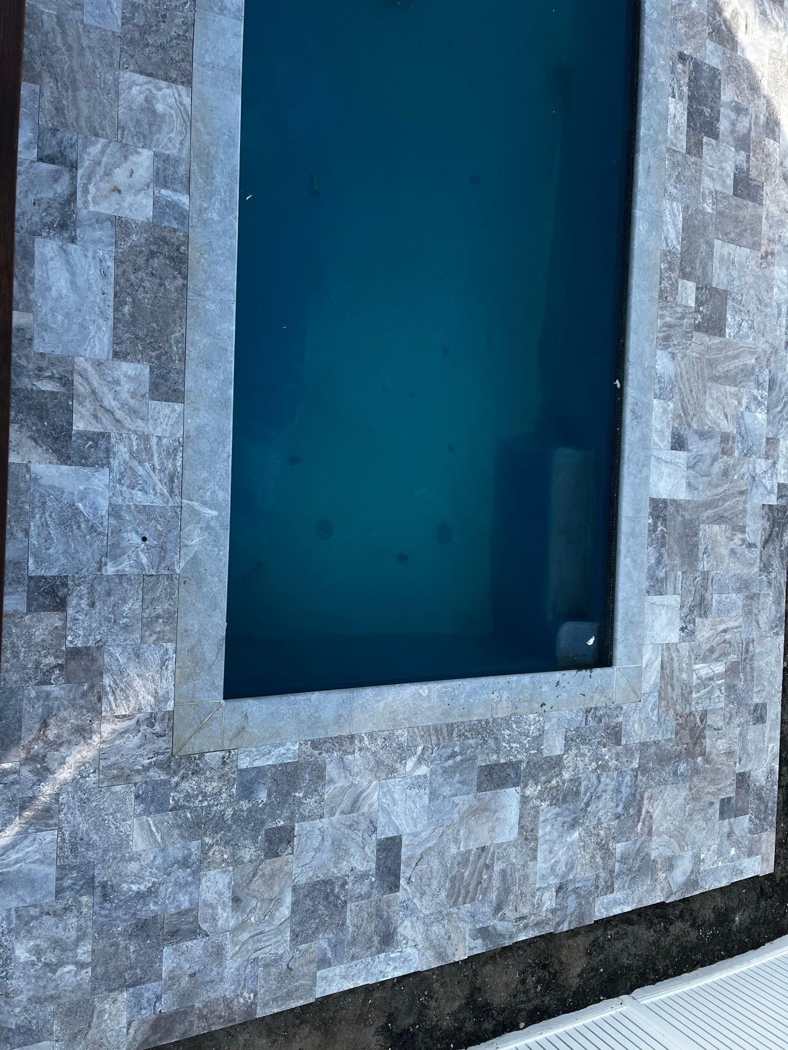 Swimming pool with gray stone border and blue-green water.