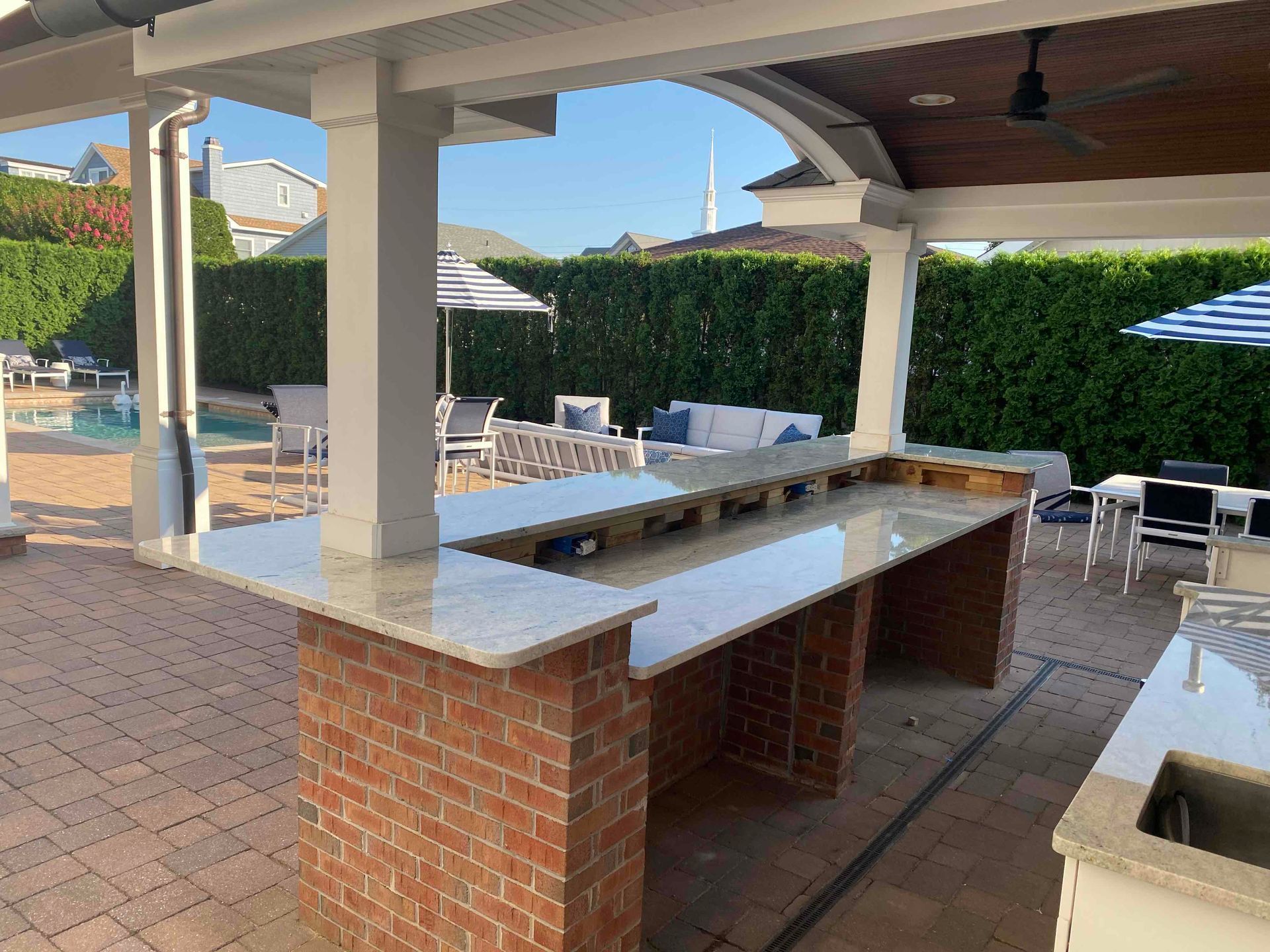 Outdoor bar with granite countertop, brick base, under a covered patio near a pool.