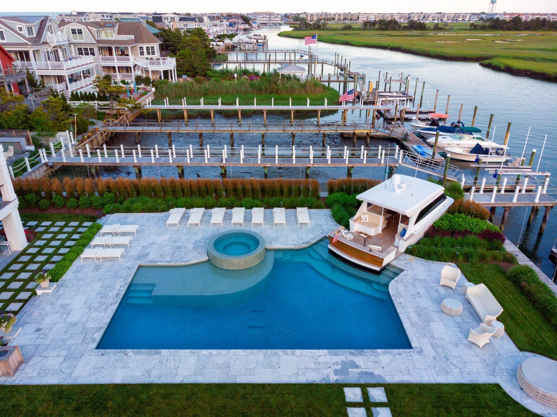 Luxurious waterfront home with pool, hot tub, boat, docks, and marsh in background.