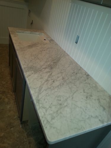 Long countertop with marble-like pattern over gray cabinets, set against white paneled wall.