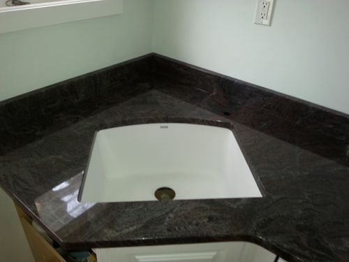 Dark brown granite countertop with white rectangular sink in corner of bathroom.