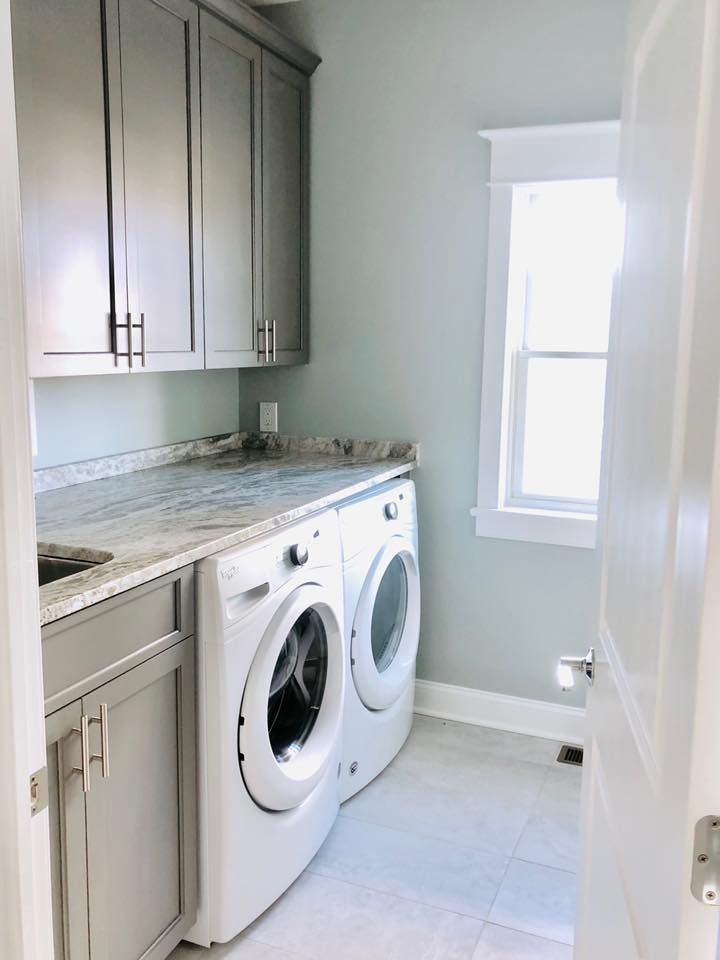 Laundry room with gray cabinets, washer/dryer, light blue walls, and window.