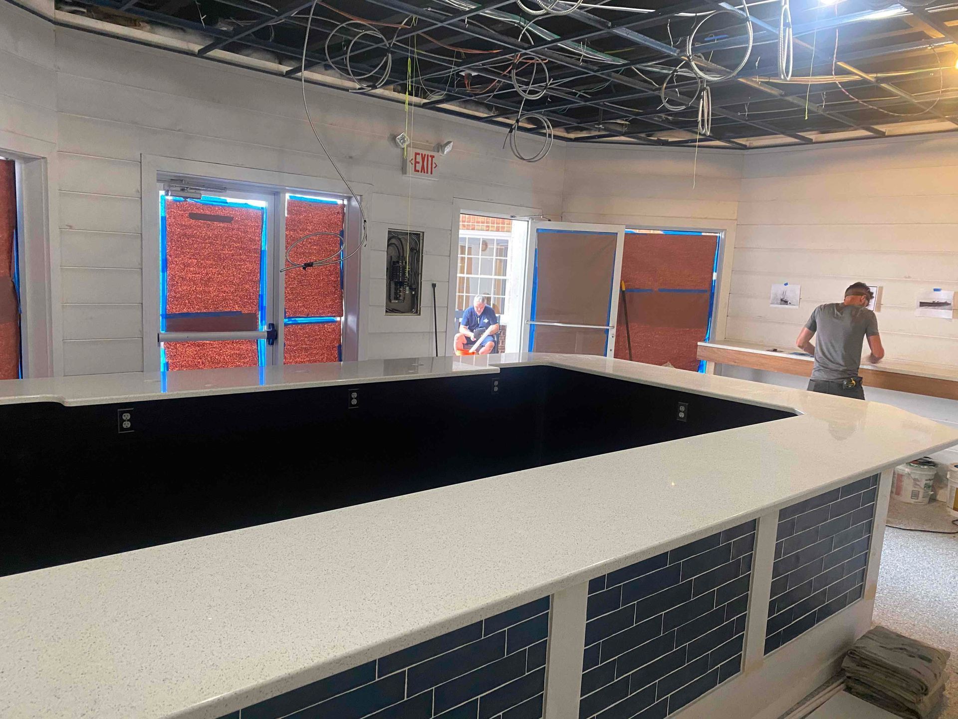 Bar under construction with white countertop, blue tile, and person working in the background.