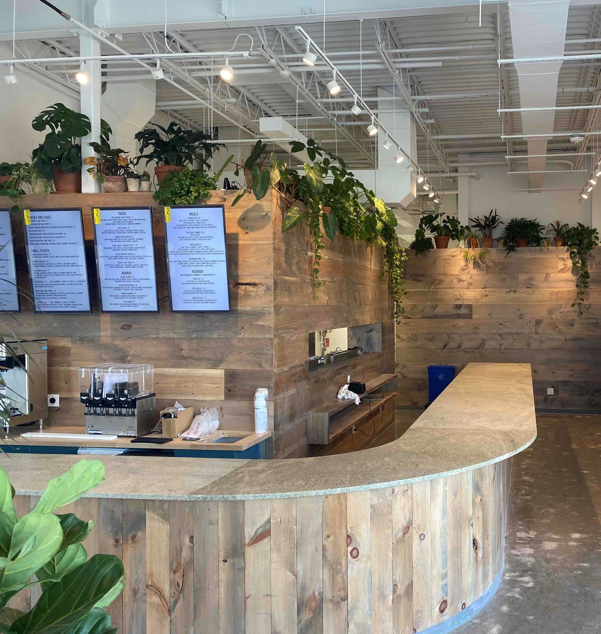 A cafe with a wooden counter and walls, plants, and a menu board.