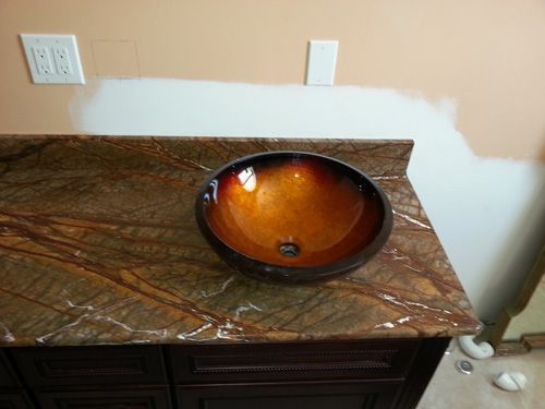 Bathroom vanity with a brown marble countertop and an orange glass vessel sink.