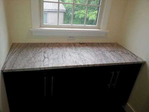 Dark cabinet with granite countertop under a window.