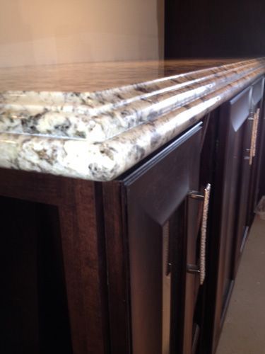 Close-up of a kitchen cabinet with a light-colored granite countertop and dark brown cabinets with silver handles.