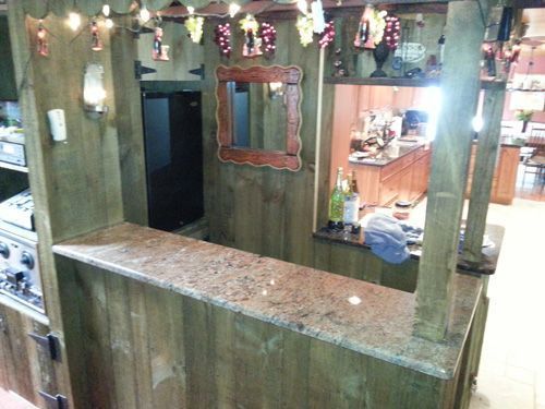 Wooden bar with granite countertop, mirror, and kitchen visible in the background. Festive decorations hang overhead.